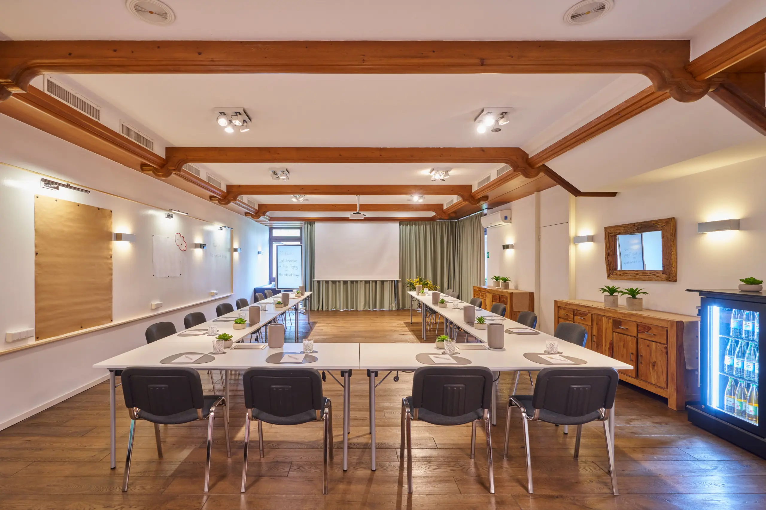 Heller Konferenzraum mit langen Tischen in U-Form und Holzdeckenbalken